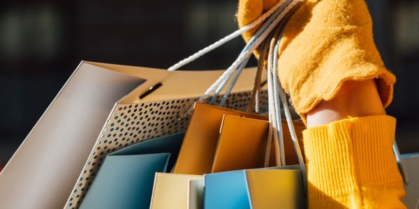 Person holding colorful shopping bags while wearing a yellow sweater.