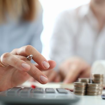 Person calculating finances with coins and a piggy bank nearby.