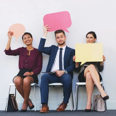 Three professionals holding colorful speech bubble signs while seated.