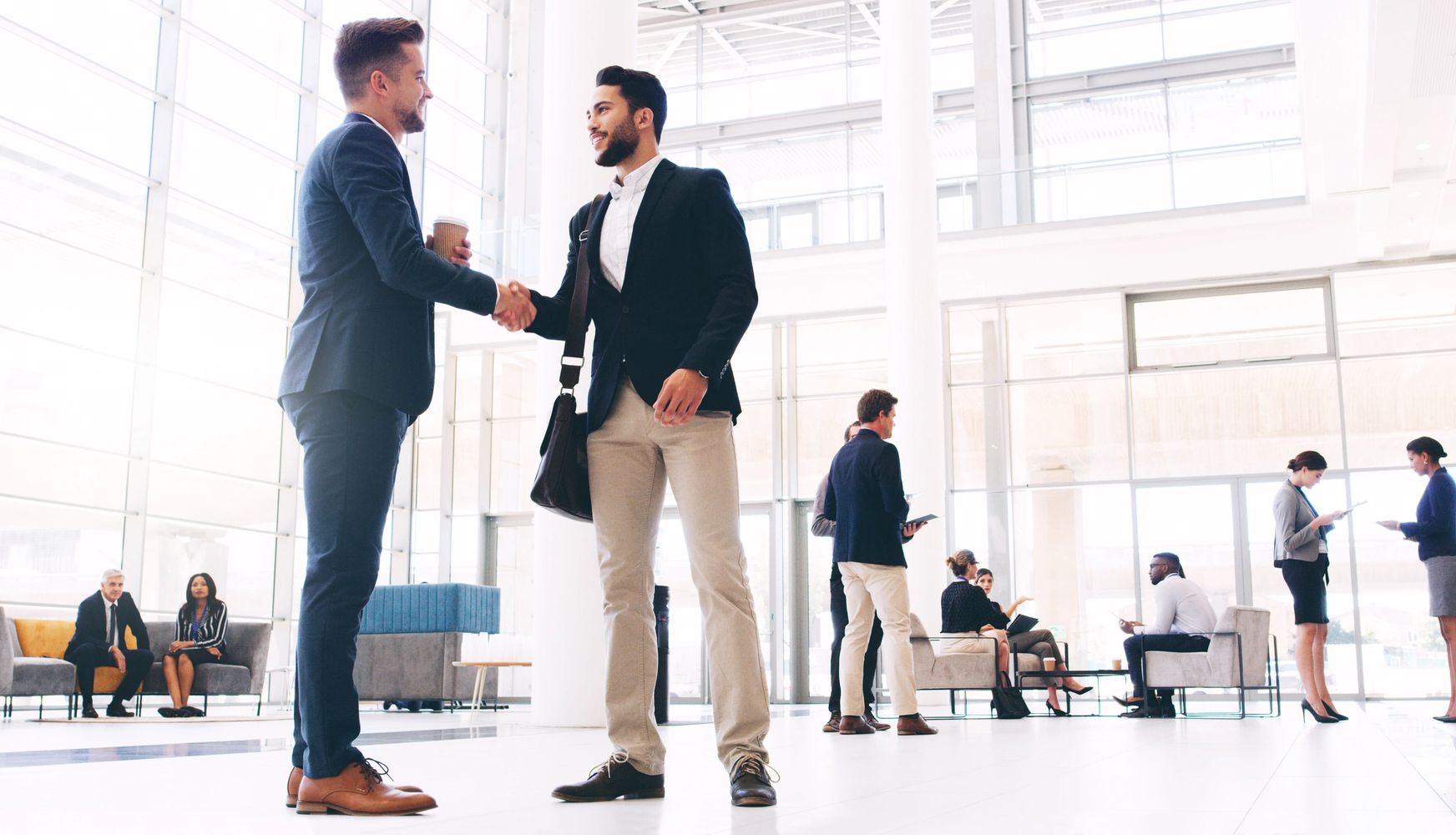 Two businessmen shaking hands in a modern office lobby.