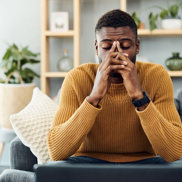 A man in a mustard sweater sitting on a couch, looking stressed and contemplative.