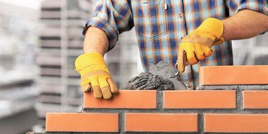 Construction worker laying bricks with mortar wearing gloves.