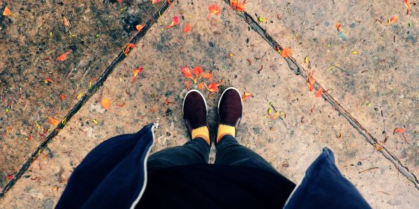 Person standing on a concrete ground with scattered red leaves.