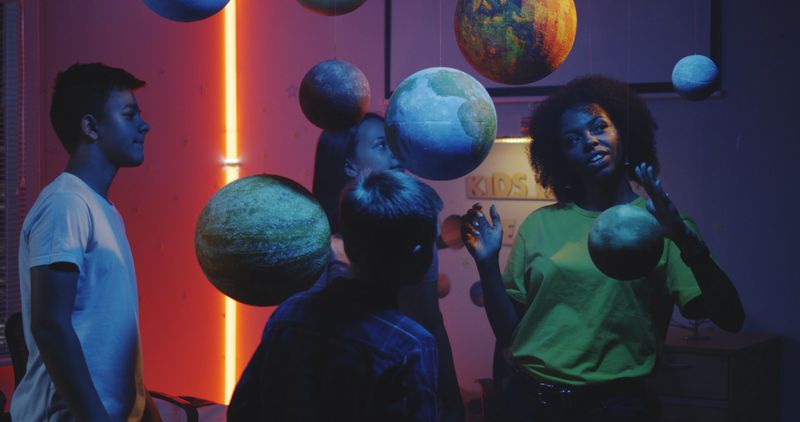 Medium shot of a young female teacher explaining astronomy to students with planet models