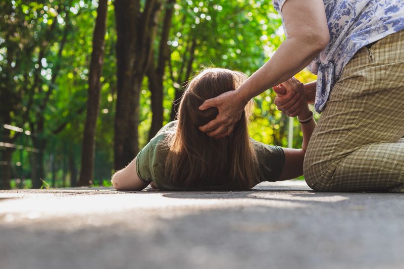 Fainted girl helped by an old woman – Teenager trying to get back on her feet while receiving support from an elder