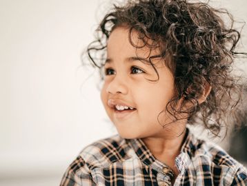 Smiling toddler with curly hair wearing a plaid shirt.