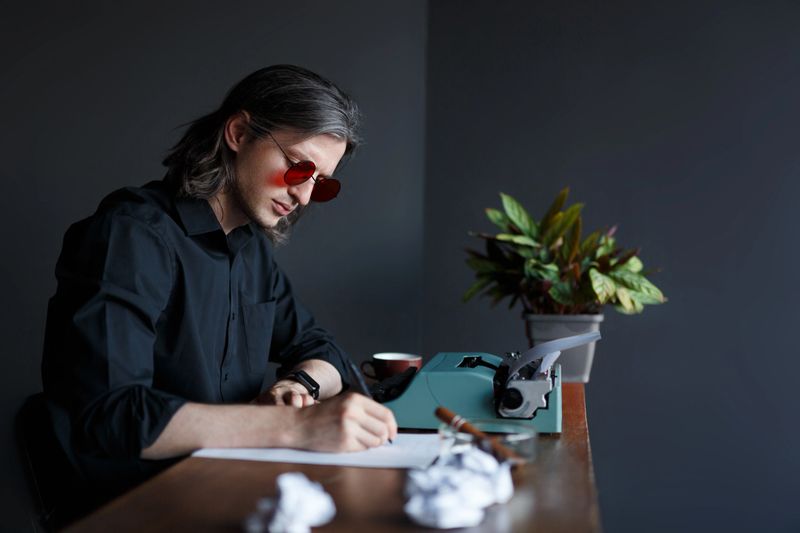 Young modern writer, working at the table, writing a letter on paper, Copy space. Vintage typewriter. Shooting in studio.