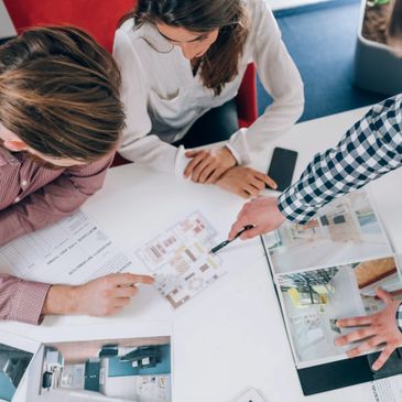 Three people discussing architectural plans and interior designs around a table.