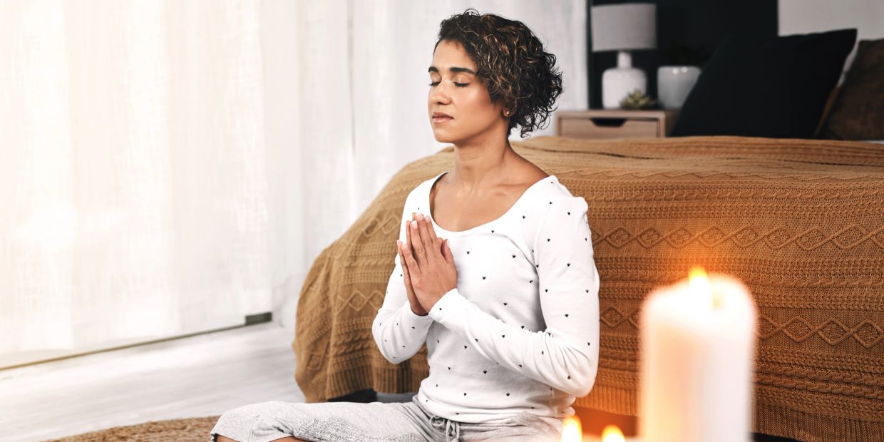 Woman meditating peacefully indoors with candles.