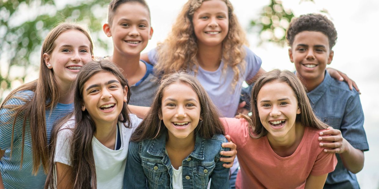 A diverse group of happy teenagers smiling together outdoors.