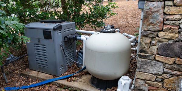 Outdoor pool pump and filter system beside a stone wall.