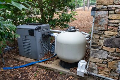Outdoor pool equipment including a pump and filter system beside a stone wall.