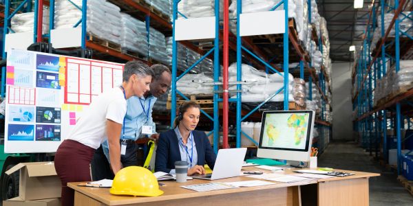 Three workers plan logistics in a warehouse.