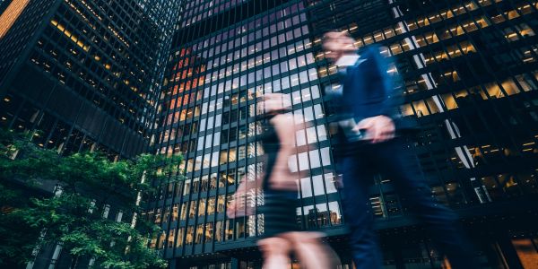 People walking quickly in front of tall office buildings in a city.