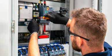 Electrician working on an electrical panel wearing gloves and safety glasses.