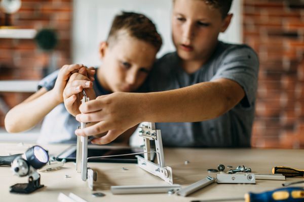 2 tween boys working together to construct project one boy helping other hand over hand support