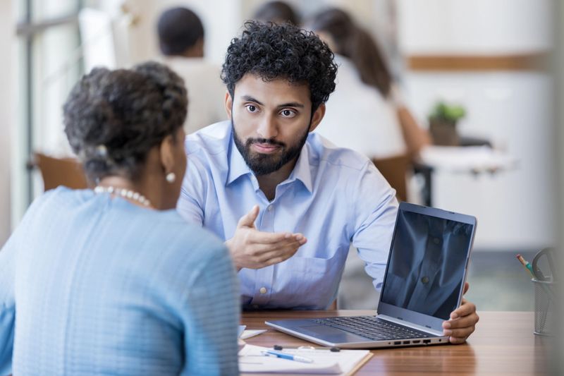 A young male financier presents his senior female client an update on the status of her organization's funds.