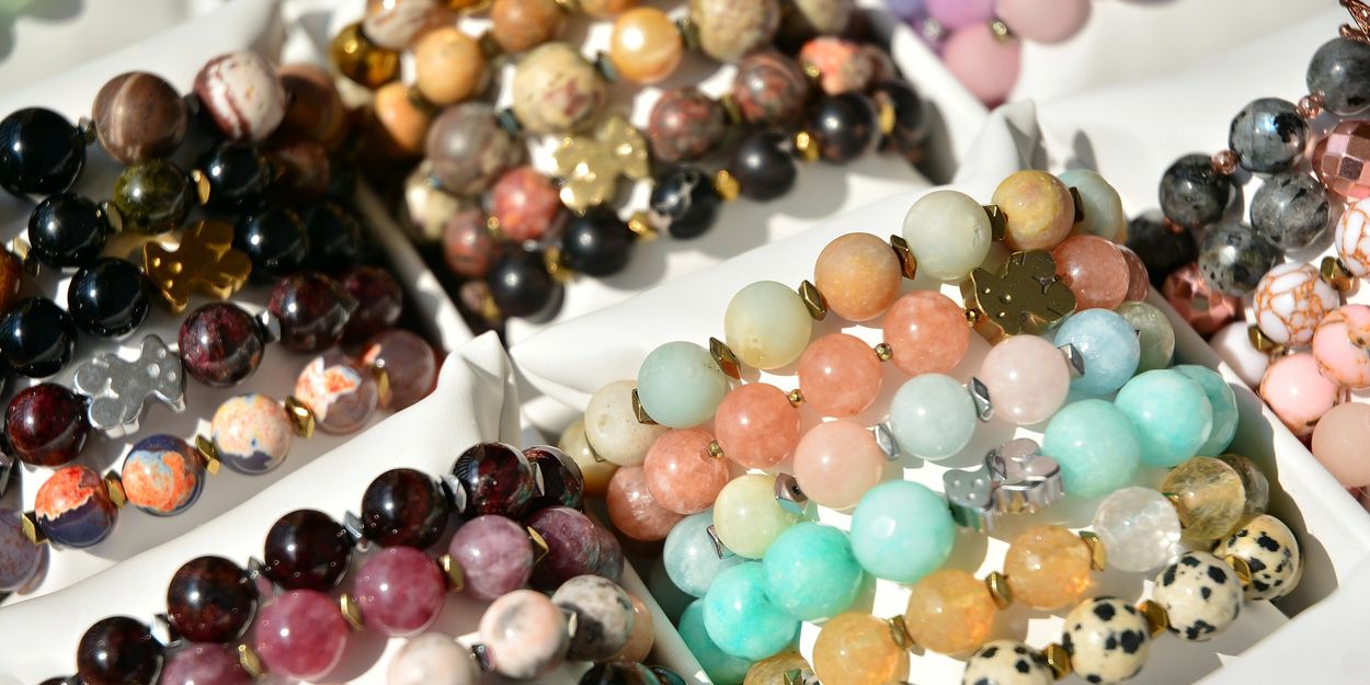 Colorful gemstone bead bracelets with metallic accents arranged in white trays.