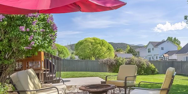Outdoor patio with cushioned chairs, a fire pit, and a large red umbrella on a sunny day.