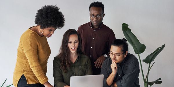 A diverse group collaborating around a laptop in an office space.