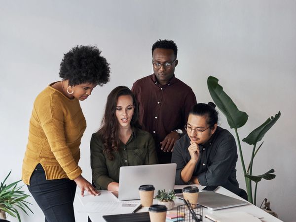 Four colleagues collaborating around a laptop in a modern office setting.