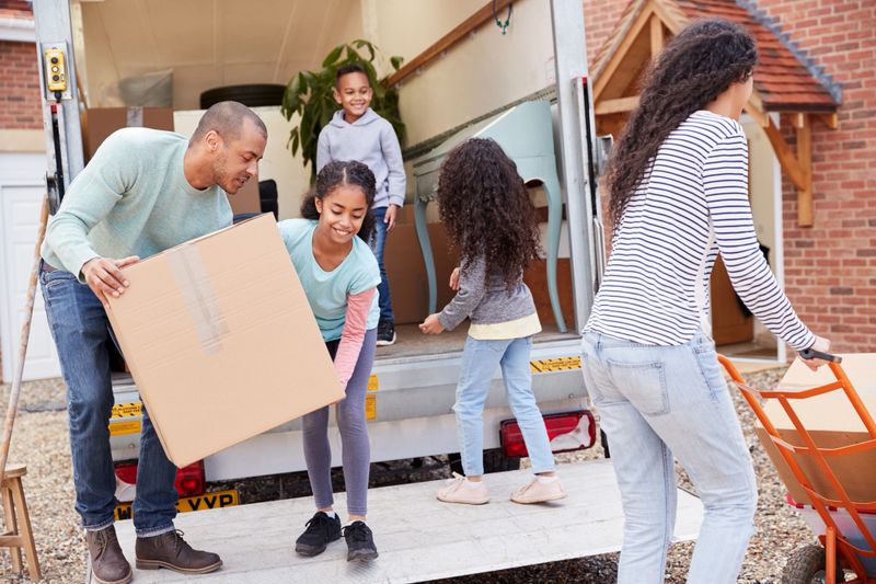 Family Unloading Furniture From Removal Truck Into New Home
