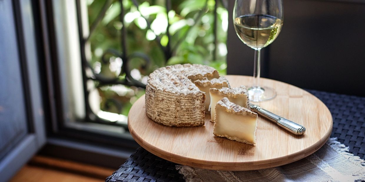 Rustic cheese wheel with slices and a glass of white wine on a wooden board.