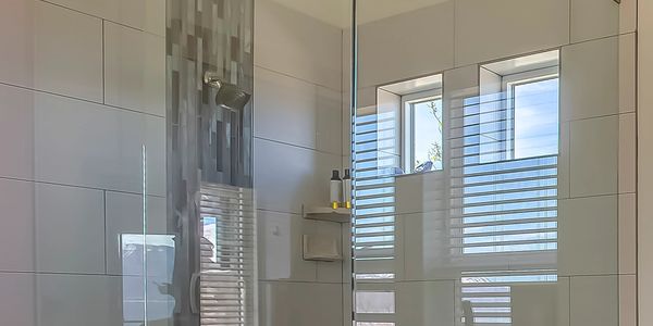 Modern bathroom shower with glass enclosure and window reflection.