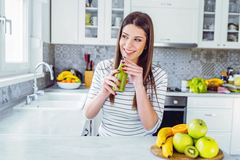 Happy teenage girl drinking smoothie on a solid color background