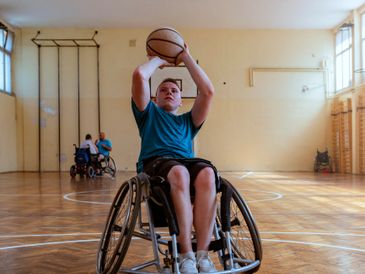 Young boy in wheelchair preparing to shoot a basketball indoors.