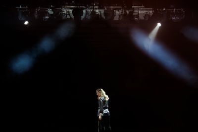 Woman in spotlight on a dark stage with a microphone stand.