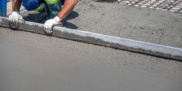 Construction worker smoothing freshly poured concrete on a rebar foundation.