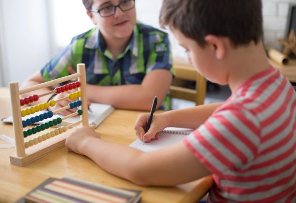 Two boys learning math with an abacus and writing notes at a table.