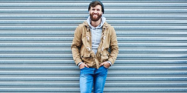 Smiling man in casual outfit leaning against a metal shutter.