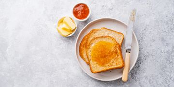 Toast with marmalade, butter, and a knife on a plate.