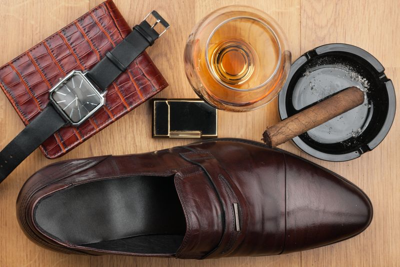 Men accessories. Brown elegant shoes, wallet, alcohol and cigar on wooden table. Top view.