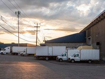 Delivery trucks parked outside a warehouse during sunset.