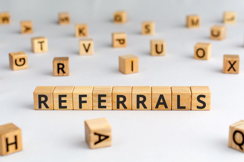 referrals - word from wooden blocks with letters, spreading referral viral  marketing concept, random letters around, white  background