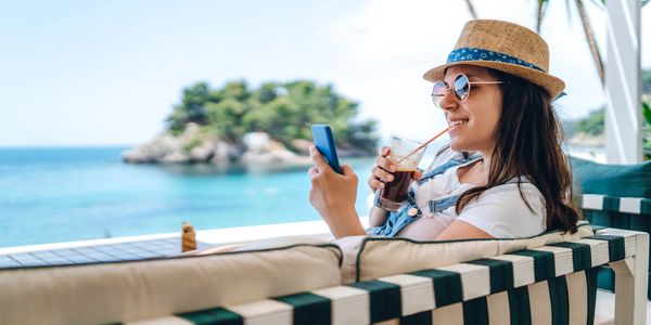 Woman relaxing by the sea with a drink and phone.