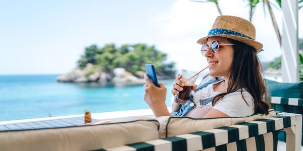 Woman relaxing by the sea with a drink and phone.