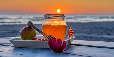 Jar of honey with apple and butterfly at sunset on the beach.