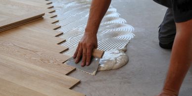 Worker installing wooden floorboards with adhesive.