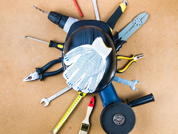 Various construction tools arranged around a black safety helmet with a work glove on top.