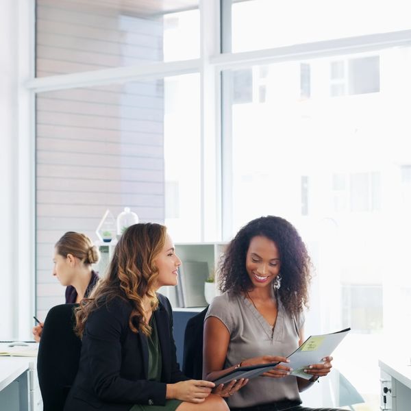 Two professional women discussing documents in a bright office.