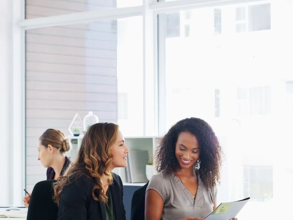 Two women discussing work documents in a bright office.