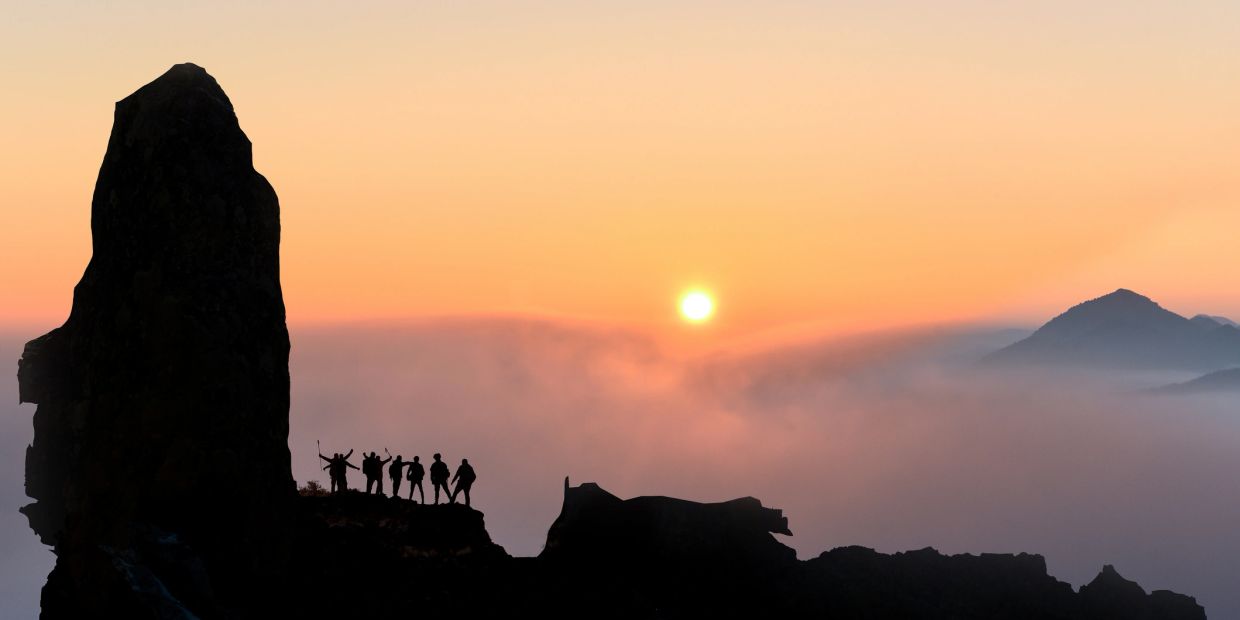 Silhouette of hikers at sunset on rocky peaks.