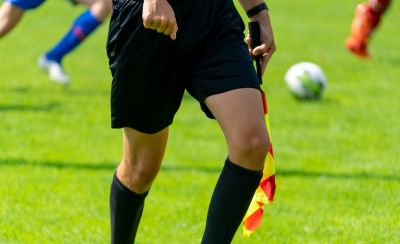 Soccer referee in black uniform with a flag on the field.