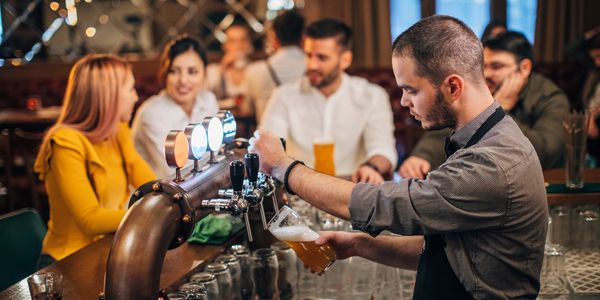 Bartender pouring beer while customers chat at a bar.