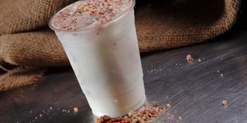 Iced nut milk drink topped with crushed pecans in a plastic cup.