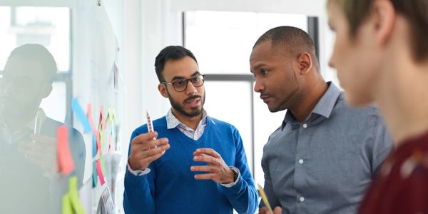 Three colleagues brainstorm ideas using sticky notes on a glass wall.